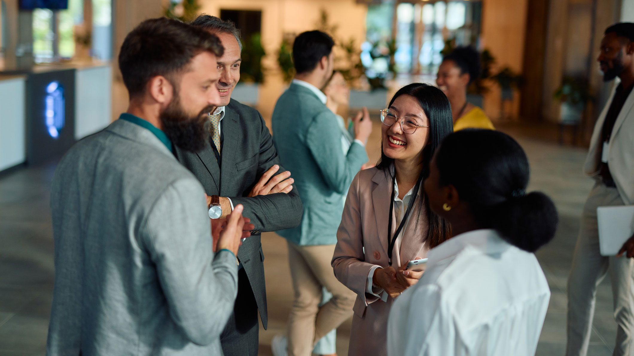 Group of multi-ethnic business professionals networking and engaging in conversations during a corporate event held in a spacious lobby, fostering connections and collaboration